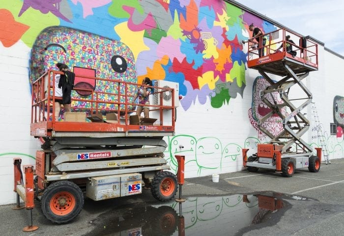 From left, Vanessa Scrivani, artist Miss Zukie, artist JPO, and RAW Arts member Michael Aghahowa work on the mural at City Hall Square during the Beyond Walls Mural Festival on Friday